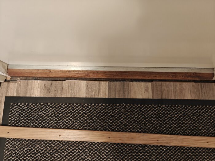 Trägolv avslutas vid dörr med trälist, visar stor springa och skruvhål på tröskel. Diskuterar möjliga lösningar för att förbättra utseendet.