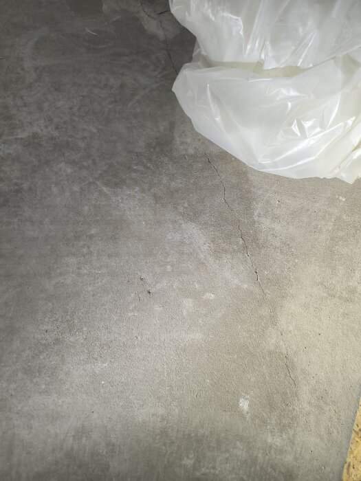Spricka i betonggolv med isolerad platta i källaren, nära golvbrunn. Plasten syns, osäker om reparation behövs innan golvläggning.