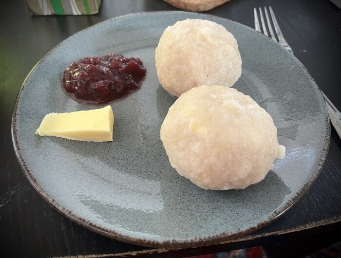 På en tallrik ligger två öländska kroppkakor med smör och lingonsylt vid sidan.