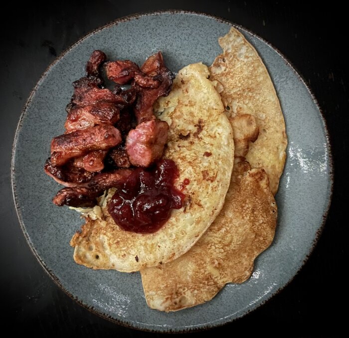 Raggmunkar med stekt fläsk och lingonsylt serverade på en tallrik.