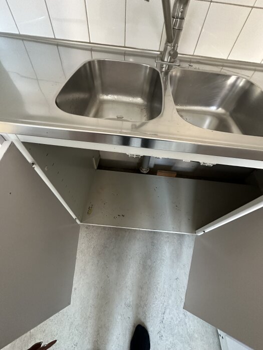 Under diskbänken i köket med dubbla hoar, skåpet är öppet för att visa utrymmet där en diskmaskin kan placeras, rör synliga.