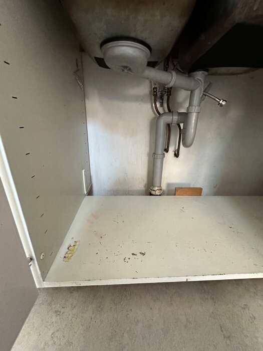 Underskåp under diskbänk med rör och tom yta för eventuell installation av bänkdiskmaskin.