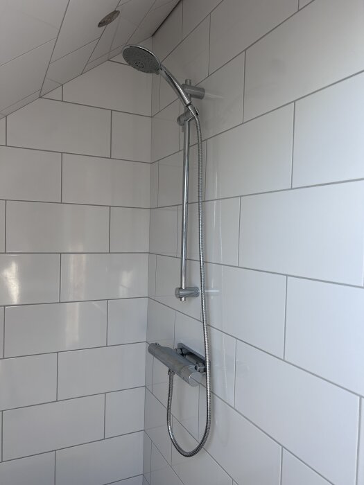 Dusch med regnduschhuvud och väggmonterad termostatblandare på vitkaklad badrumsvägg.