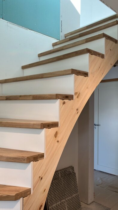Trätrappa i birk med vitmålade sättsteg och dolda vangstycken, placerad i ett byggprojekt med fokus på inredning och avslutande detaljer.