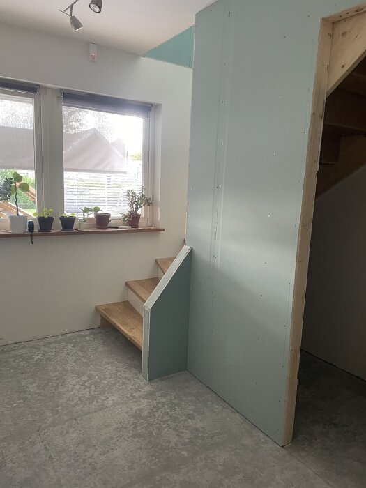 Trappa inomhus bredvid fönster med krukväxter och byggd halvvägg i grönt i färdigt rum.