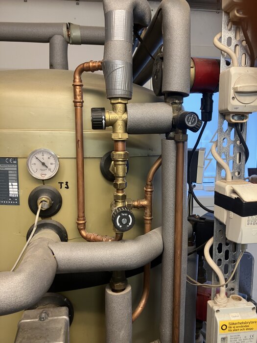 Vattenvärmesystem med kopparrör och isolering, visar två blandningsventiler och en temperaturmätare.