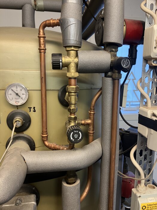 Värmesystem med kopparrör, termostatventiler och temperaturmätare i ett pannrum.