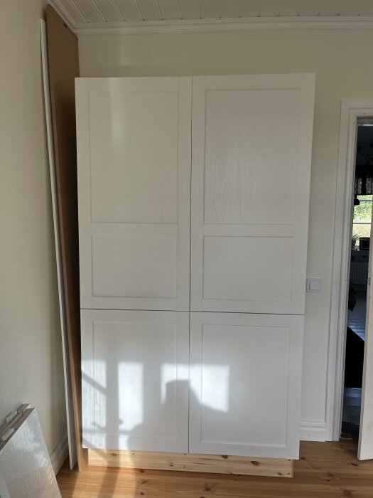 Vitt förvaringsskåp med fyra dörrar och träådring, monterat i ett rum med trägolv och ljus vägg.