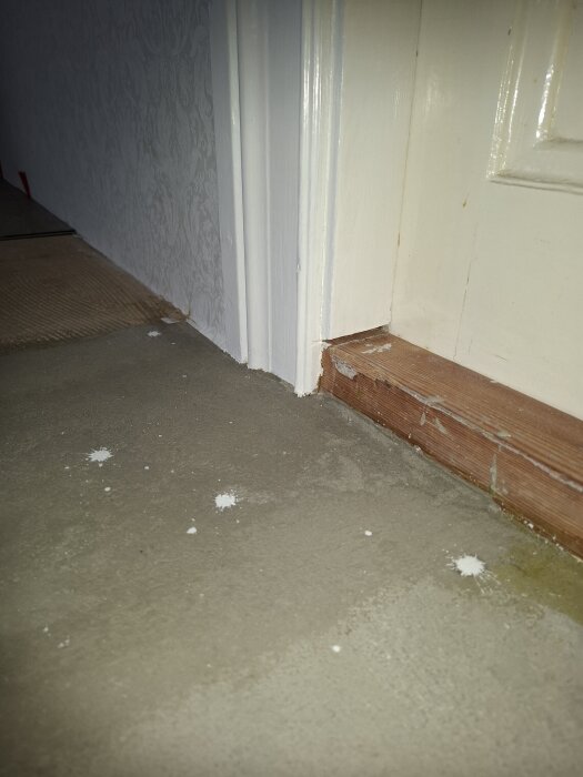 Tröskel och oregelbundet golv med vitt stänk, visar problem med golvläggning och behov av justering eller användning av list.