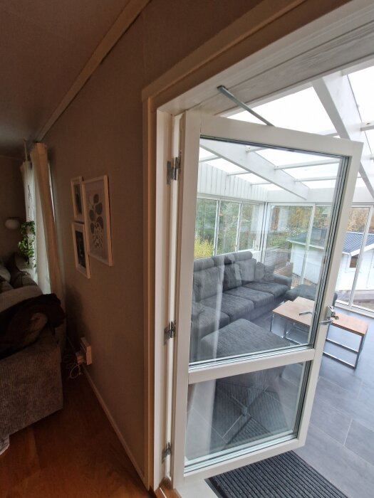 En vit altandörr med glas är öppen mot ett uterum med soffor, synlig glipa i övre hörnet.