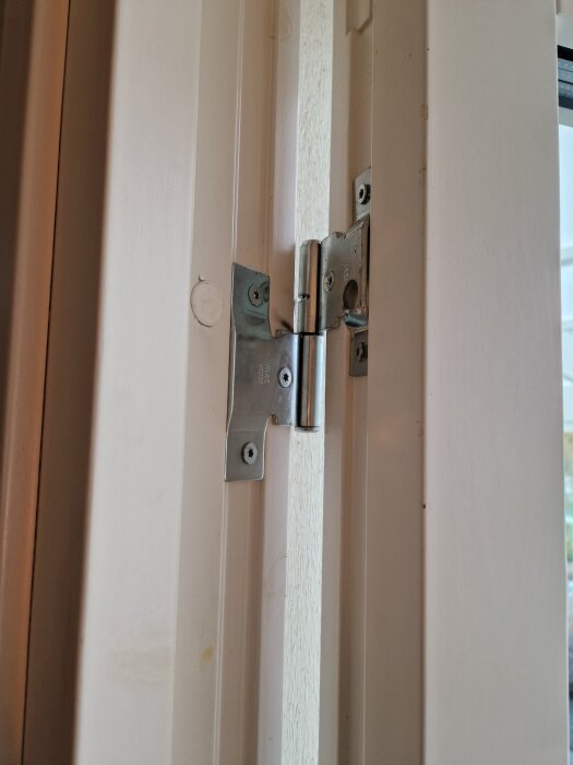 Gångjärn på en vit altandörr av modell Assa 3210, visar justeringspunkter och möjliga glipor i dörrkarm.