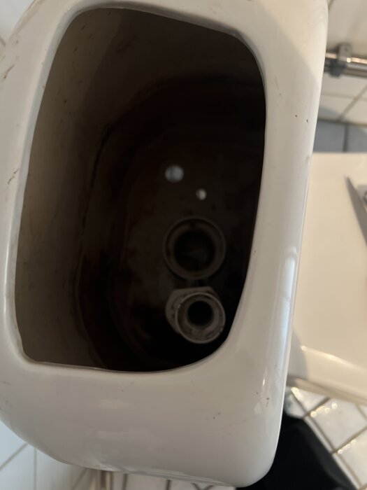 Toalettcisterns insida visas uppifrån, med två synliga röröppningar och skugga på insidan.