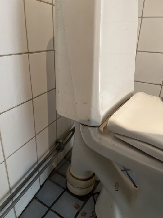 Toalettens undersida och vattenbehållare med kakelvägg och golv i bakgrunden.