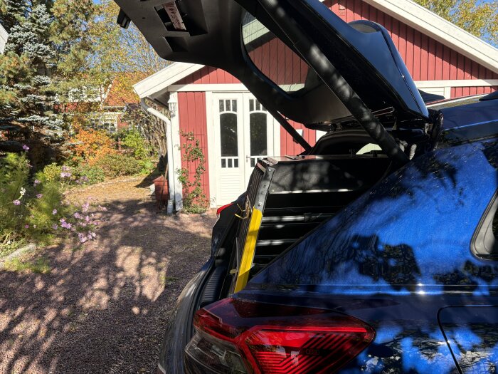 Audi Q4 e-tron med öppen baklucka, visar otillräckligt utrymme för en 80 cm djup bur på en gård med rött hus i bakgrunden.