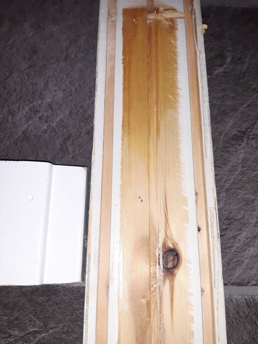 Insidan av en gammal dörrkarm med små hål efter häftklamrar och borttagen träskiva, synliga träfibrer och träknut.