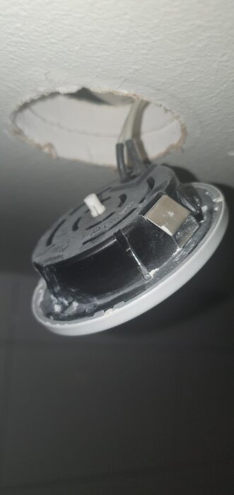 Bilden visar en spotlight som hänger från taket med synliga kablar. Det finns en pilmarkerad glasdel på spotten i ett badrum.