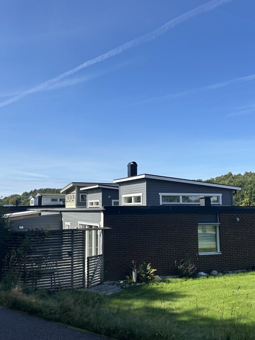 En enplansradhus med platt tak och atriumgård, omgiven av grönskande trädgård under klarblå himmel.
