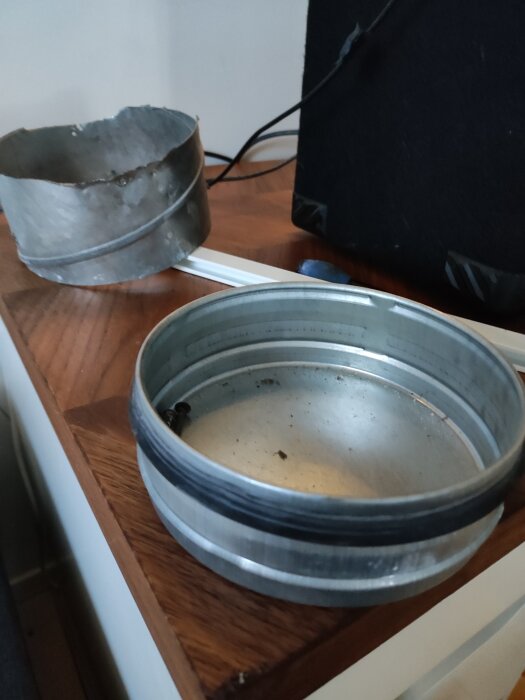 Ett metalländlock och en avklippt rörbit ligger på ett träbord.