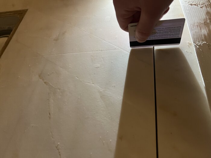 En hand håller ett kort ovanför skarven mellan två stenar på duschgolvet för att mäta höjdskillnad.