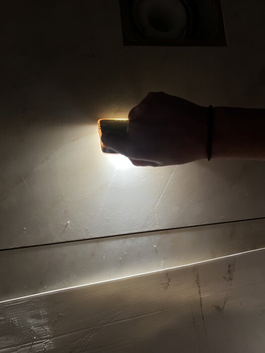 En hand håller en ljuslampa mot nyinstallerade stenplattor i duschen, visar nivåskillnad på millimeter mellan plattorna.