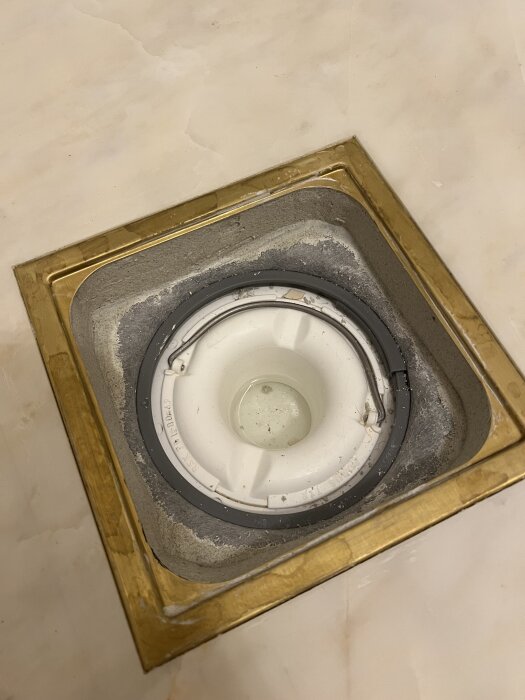 En nyinstallerad brunn med vit plast och metallram på golv, omgiven av fyrkantigt metallgaller.