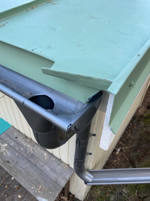 Grönt tak med ny plåt runt hörnet och stuprör; ny plasttakränna installerad. Notera målat trä samt avlägsnat ruttet hörn.