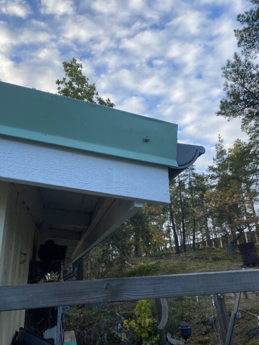 Vindskivor och takkant efter reparation, nymålade i grönt och vitt; synliga detaljer av tak och omgivande träd.