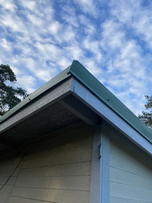 Nyinstallerade och målade vindskivor på ett tak, med fokus på hörnet som reparerats och falsats, under en blå och molnig himmel.