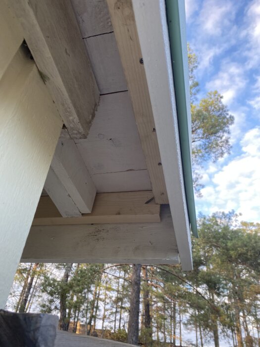 Utbytta och målade vindskivor samt takdetaljer av en plåtfirma, med träd och himmel i bakgrunden.