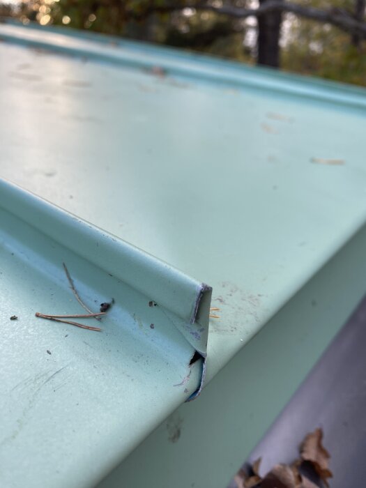 Takplåt med ny falsning, några barr på ytan och en synlig glipa vid kanterna. Hittad efter plåtfirma bytt vindskivor och reparerat hörn.