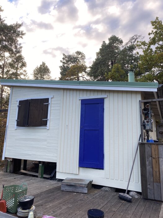 Vit byggnad med blå dörr, nybytta vindskivor och målning. Nya hörn utan röta. Glipa mellan skorsten och stöd synlig på taket.