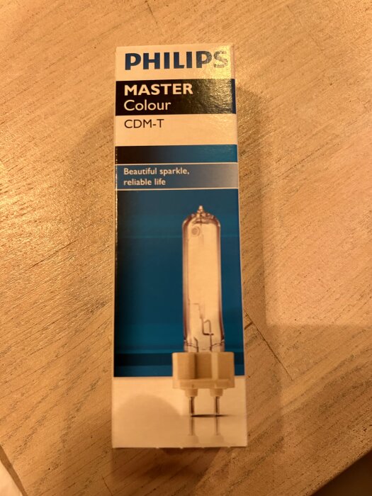Förpackning av en Philips Master Colour CDM-T lampa mot en träyta.