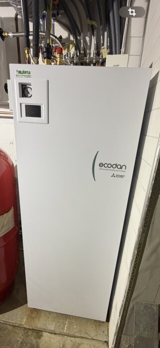 Luft/vattenvärmepump installerad i ett rum med olika kablar och anslutningar upptill.