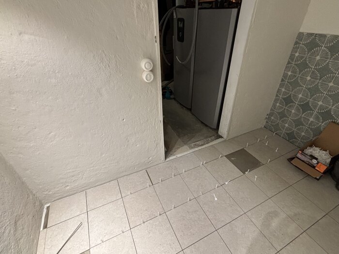 Rum med golvklinkers under installation, distanser synliga mellan plattorna, kartong med material bredvid, förbereder för fogning.