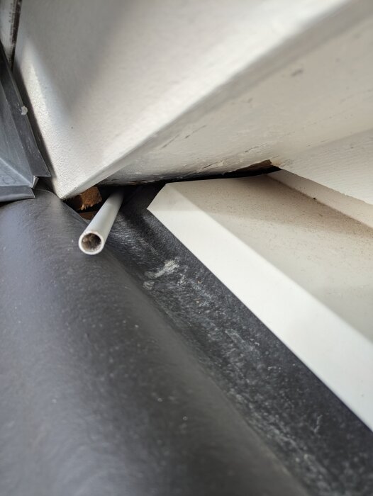 Takkupa med otätt hörn, tumstock/vp-rör sticker ut genom hålet. Uppvikt papp mot fasad; underbeslag syns, antydan till otätning i hörnet.