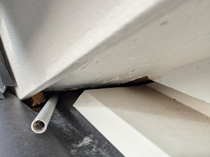 Tak med otätat innhörn vid takkupa, tumstock/vp-rör sticker ut som visar problemet, svarta och vita takmaterial synliga.