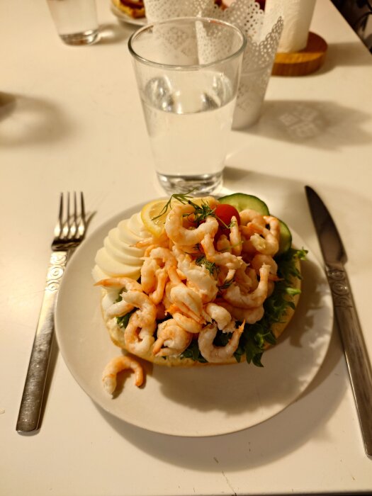 Räkmacka med ägg, citron och dill på en tallrik, bredvid ett glas vatten, kniv och gaffel.
