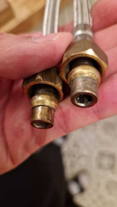 Närbild av två metallkopplingar och anslutna flexibla slangar, hållna i en hand, visar klämringar på röranslutningar.