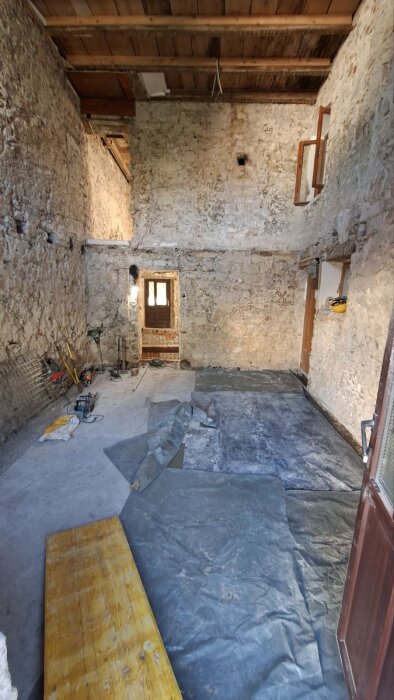 Renoveringsprojekt där bjälklag avlägsnats, rum med stenväggar, verktyg och skydd på golvet. Limträbalkar väntas.