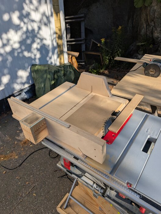 Bilden visar en cirkelsåg med en träjigg för att kapa MDF-skivor. Sektionsvis ljus och skuggor på ett utomhusarbetsbord.