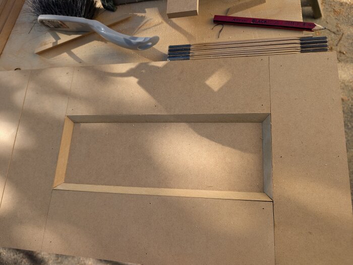 MDF-skiva med utsågade delar och verktyg som pensel och blyertspenna på en arbetsbänk.