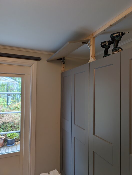 Överskåp byggs ovanpå PAX-garderober med mdf och träreglar. Två skruvdragare visas ovanpå skåpen under konstruktion.