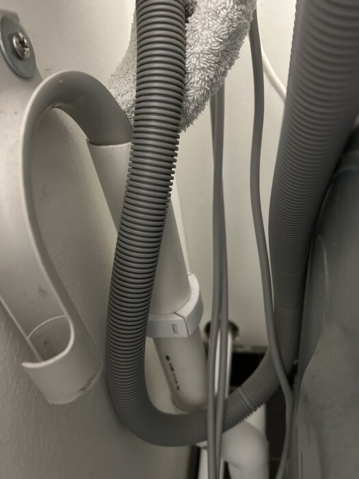 Grått avloppsrör från tvättmaskin, handduk runt röret, saknar vattenlås vilket orsakar dålig lukt, ska kopplas till avsedd röranslutning.