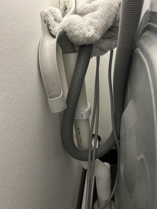 Tvättmaskinens avloppsslang kopplad till ett rör utan synligt vattenlås, med en handduk på toppen för att dölja luktproblem.