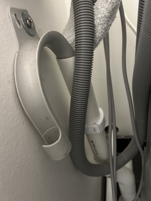 Tvättmaskinens avloppsrör som leder till ett avloppsrör, med en handduk hängande över för att dämpa stänk; vattenlås saknas.