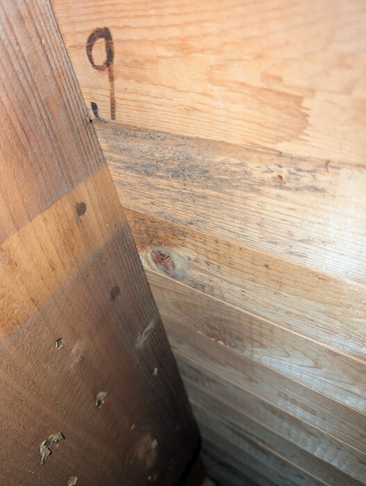 Svarta missfärgningar på träskivor nära ett hörn i en vinden, eventuella tecken på tidigare fuktproblem kring takbjälkar nära en murad skorsten.