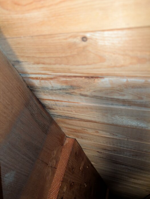 Svart missfärgning synlig på trä kring takbjälkar nära skorsten, troligen torr och inte mjuk, eventuellt indikerande problem med plåt runt skorsten.