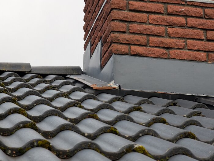 Svart missfärgning runt takbjälkar nära skorstenen, synligt på tegeltak; potentiell fuktproblem inför solpanelinstallation.