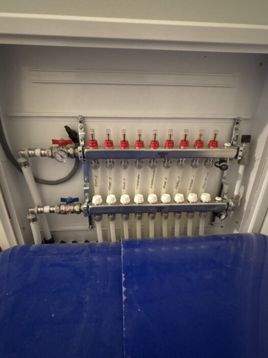 Fördelarskåp med vattenmätare och tio röda flödesmätare för golvvärmesystem. Inga ställdon synliga för individuell justering.