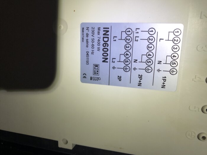 Etikett på induktionshäll med teknisk information och kopplingsschema, tydligt synlig under enhetens hölje.